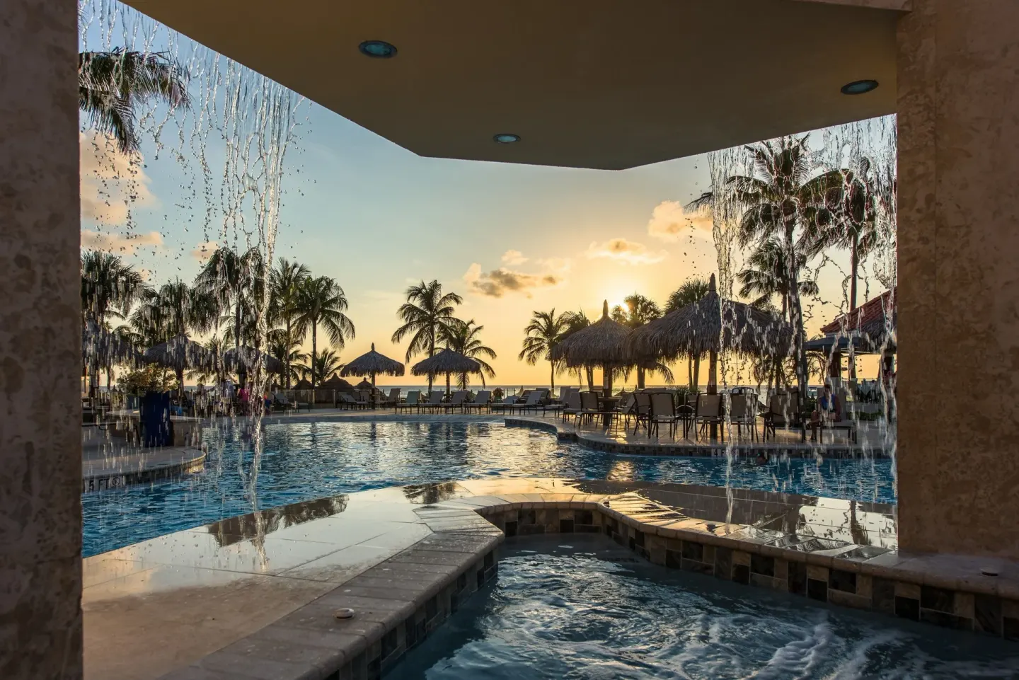 Sunset pool view with water features, palapas, and palm trees at Playa Linda Beach Resort.
