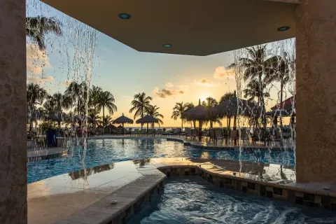 Sunset pool view with water features, palapas, and palm trees at Playa Linda Beach Resort.