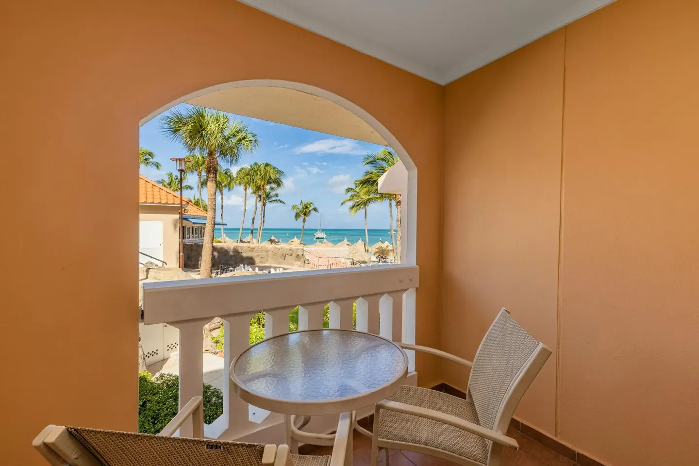 Arched balcony with table and chairs overlooking palms and the sea from the One Bedroom Suite at Playa Linda Beach Resort.