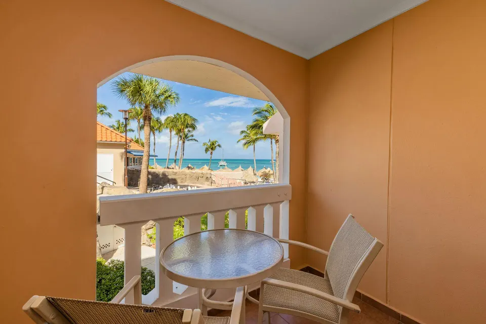 Arched balcony with table and chairs overlooking palms and the sea from the One Bedroom Suite at Playa Linda Beach Resort.