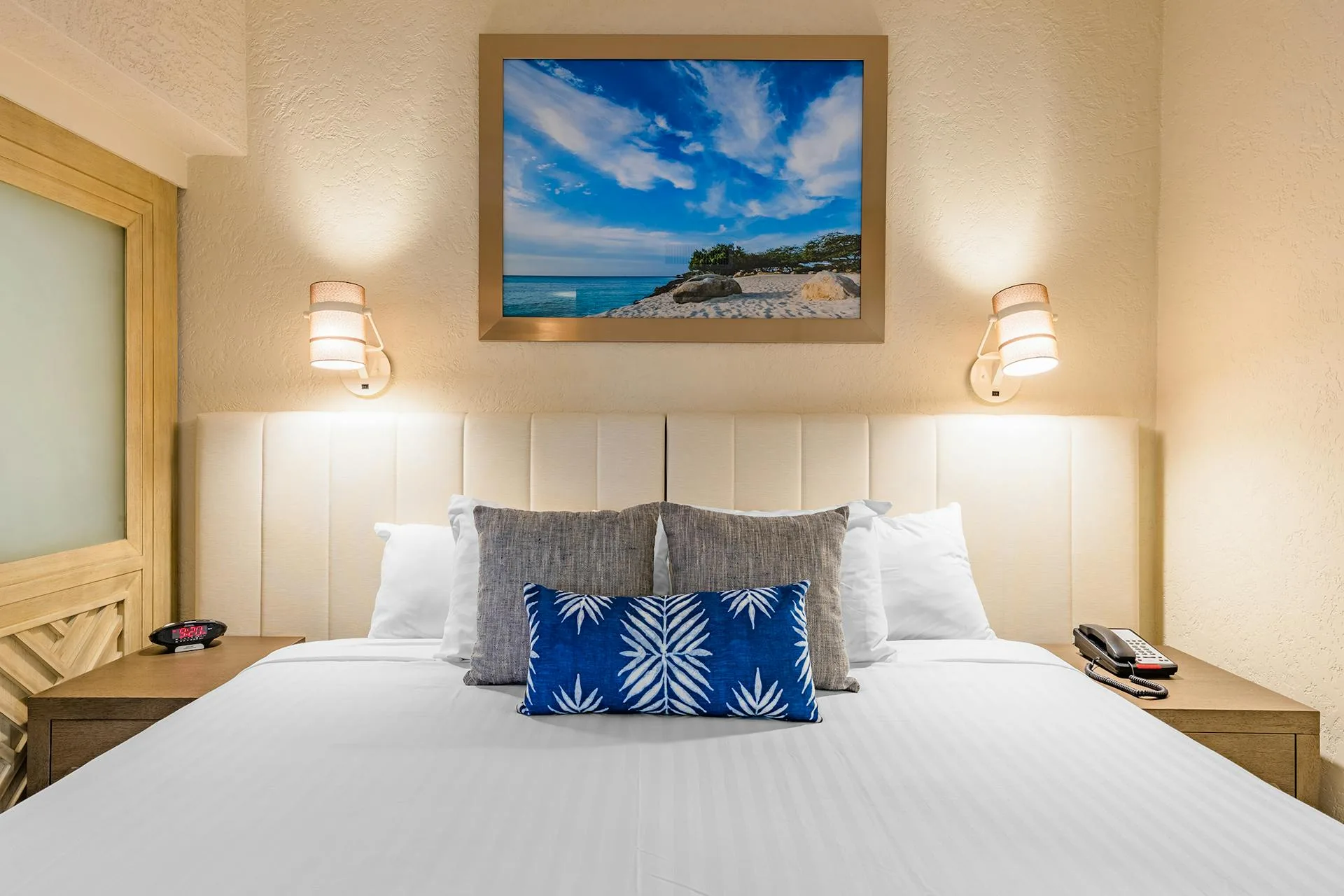 Studio Suite bed with upholstered headboard, beach artwork and reading sconces at Playa Linda Beach Resort.