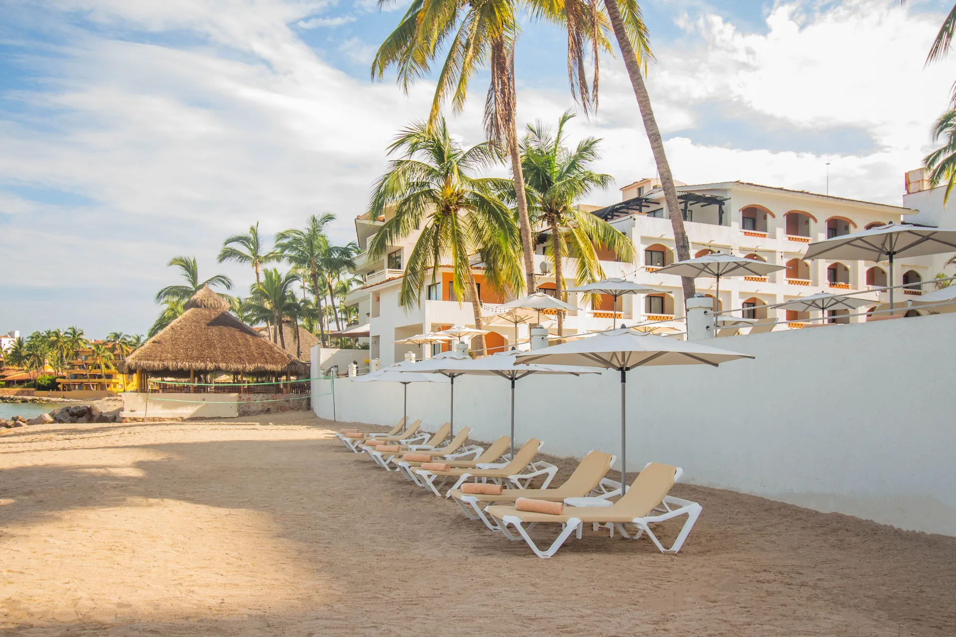 Beach loungers, umbrellas, palms, and resort building at Plaza Pelicanos Club Beach Resort.