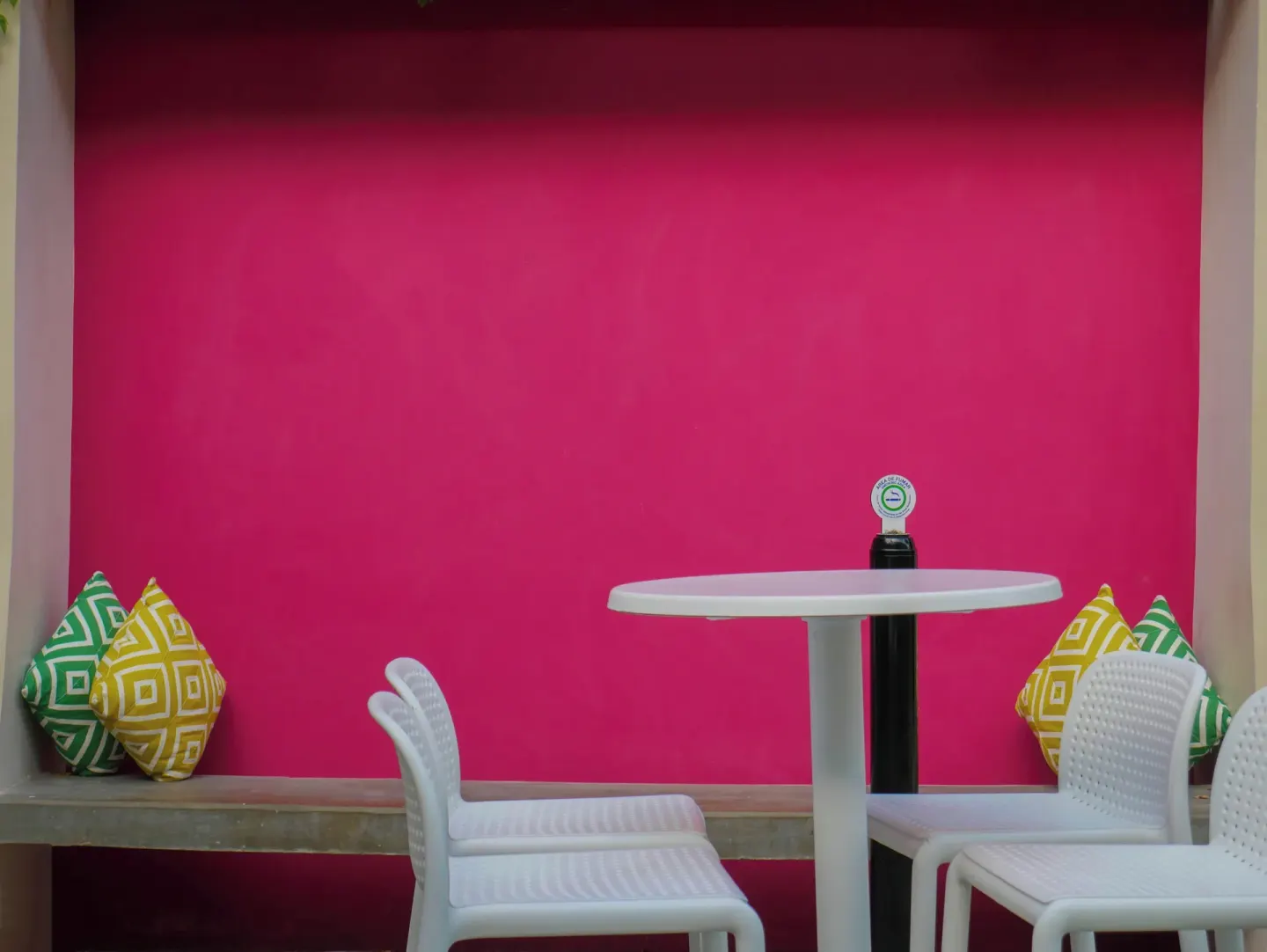 Small seating nook with white chairs and a pink wall at Plaza Pelicanos Club Beach Resort.