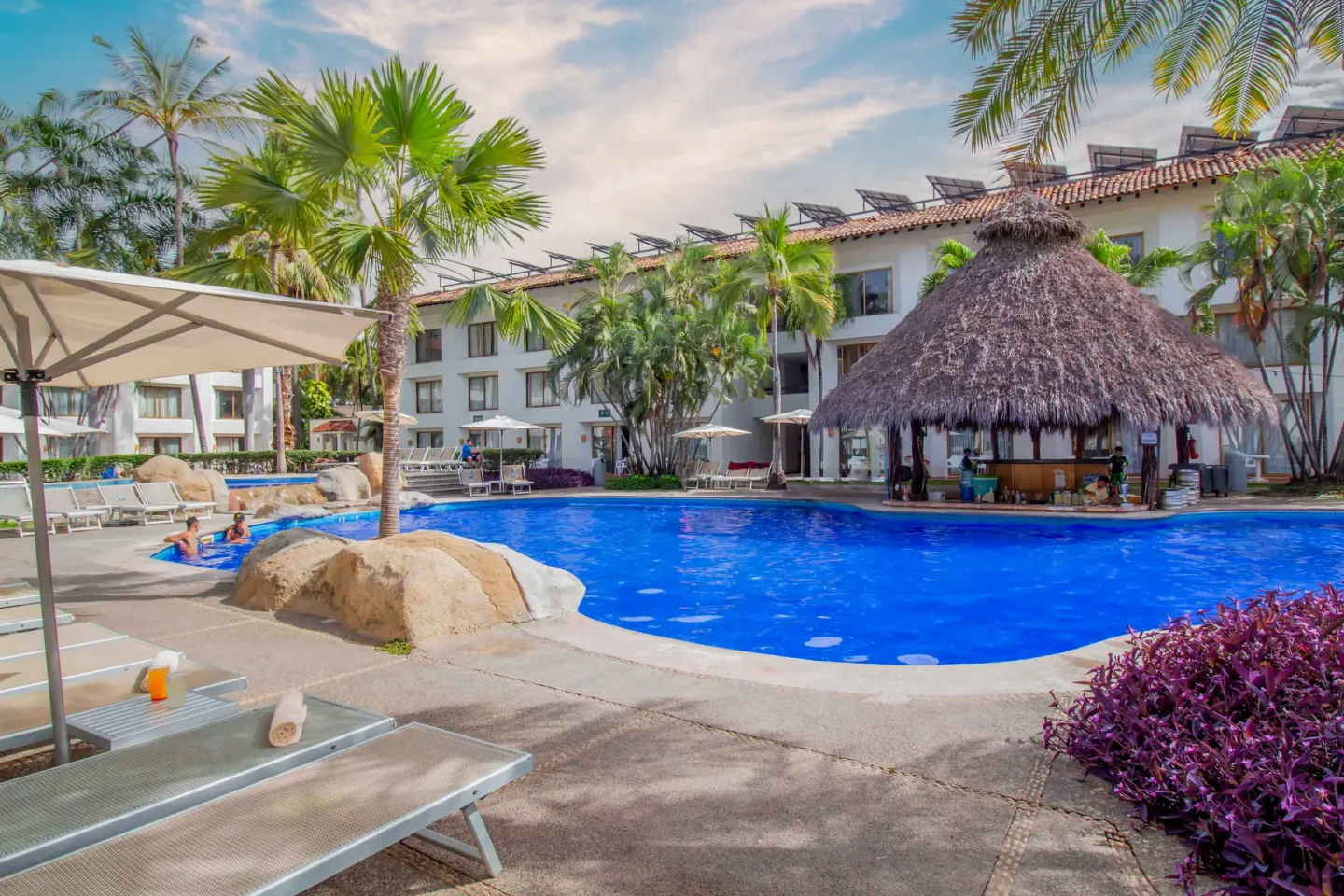 Courtyard pool with loungers and a thatched palapa at Plaza Pelicanos Club Beach Resort.