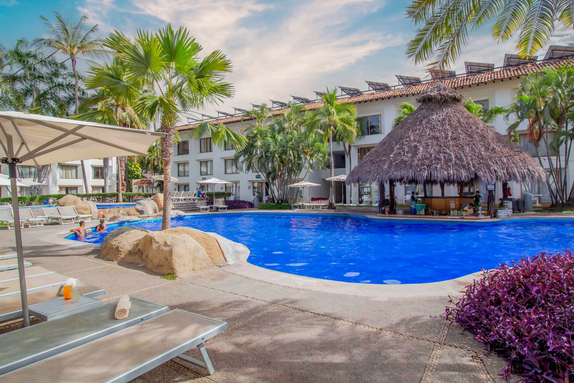 Courtyard pool with loungers and a thatched palapa at Plaza Pelicanos Club Beach Resort.