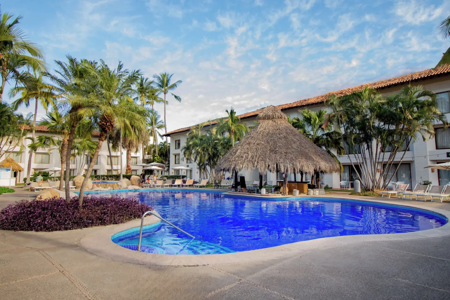 Curved pool with palms and a large thatched palapa at Plaza Pelicanos Club Beach Resort.