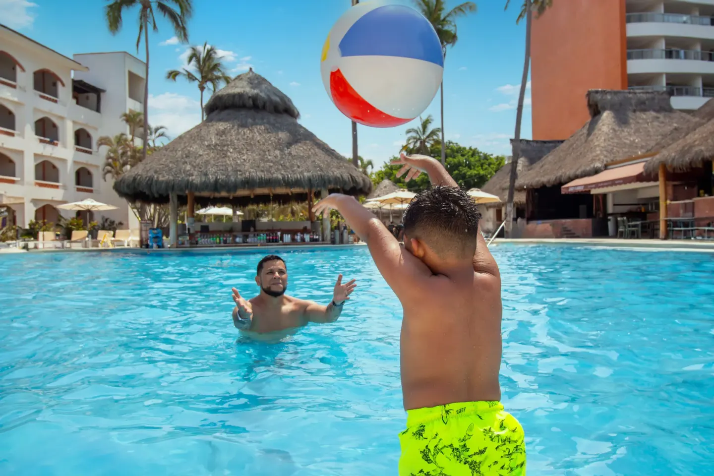 Adult and child playing with a beach ball in the pool at Plaza Pelicanos Club Beach Resort.