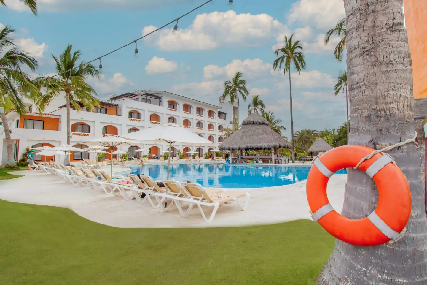Pool deck at Plaza Pelicanos Club Beach Resort with loungers, palms, and an orange life ring.