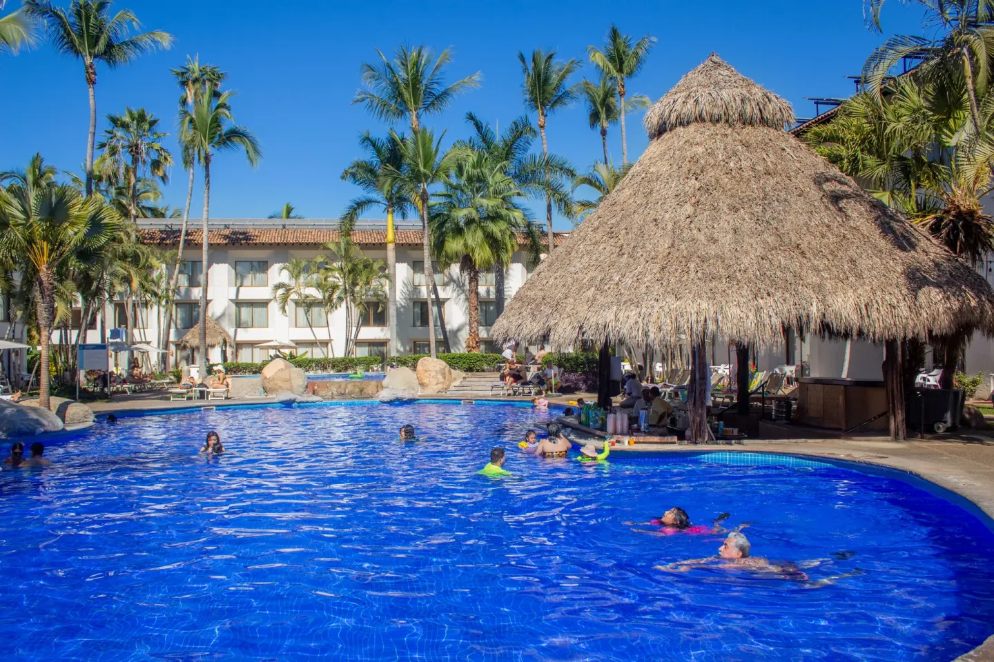 Guests swimming by a thatched palapa pool bar at Plaza Pelicanos Club Beach Resort.