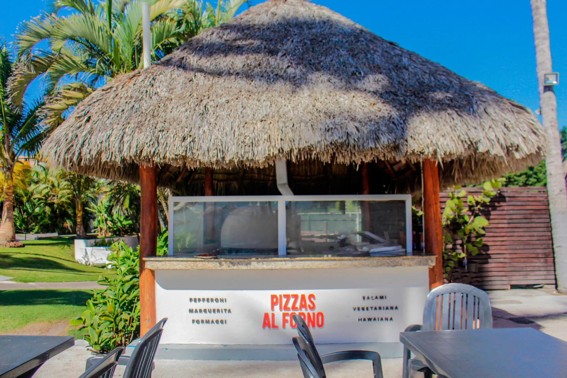 Thatched Pizzas Al Forno counter at Plaza Pelicanos Club Beach Resort with outdoor tables.