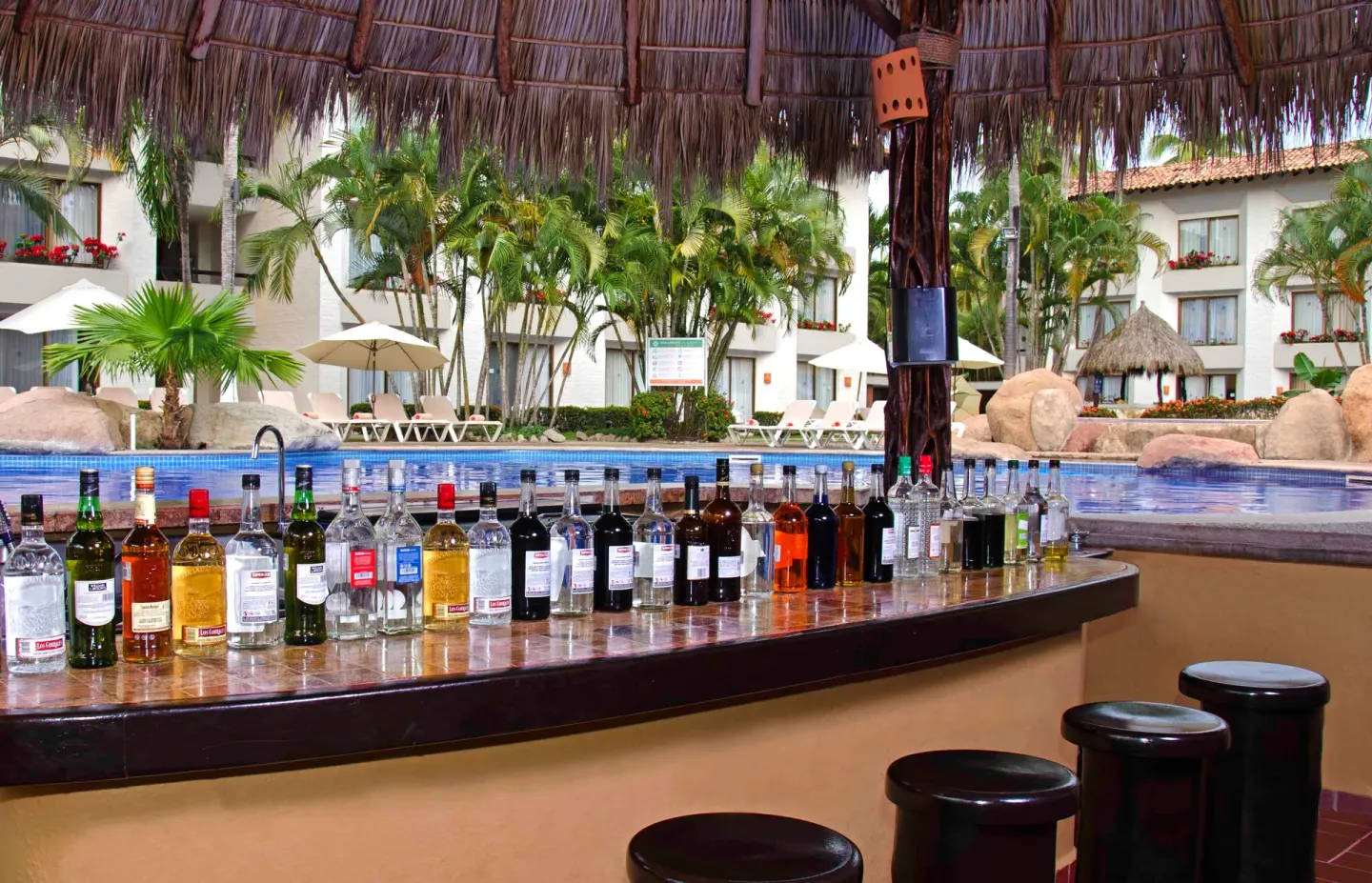Thatched pool bar at Plaza Pelicanos Club Beach Resort with stools, bottles, and pool views.