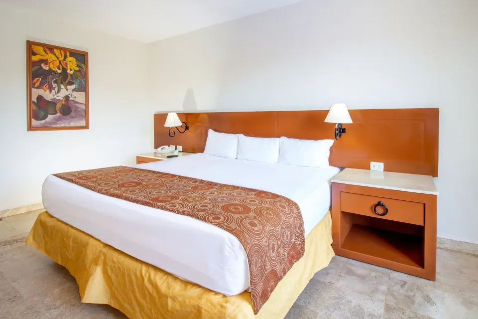 Standard room king bed with headboard and wall lamps at Plaza Pelicanos Club Beach Resort.