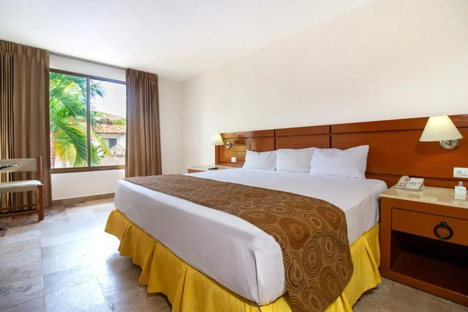 Standard room king bed beside a large window at Plaza Pelicanos Club Beach Resort.