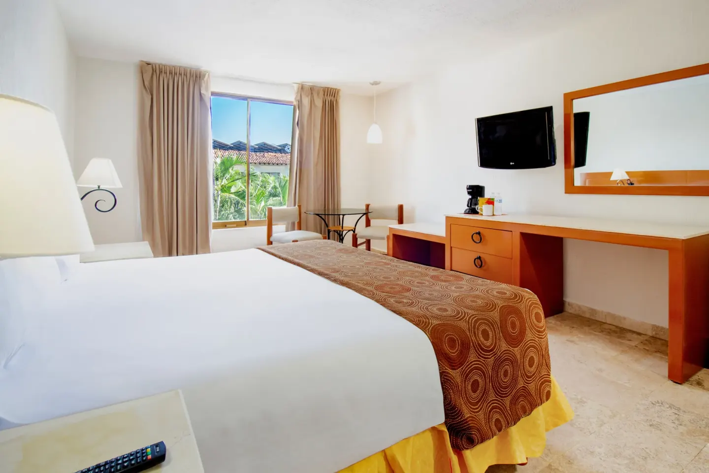 Standard room king bed, TV, mirror, and window at Plaza Pelicanos Club Beach Resort.