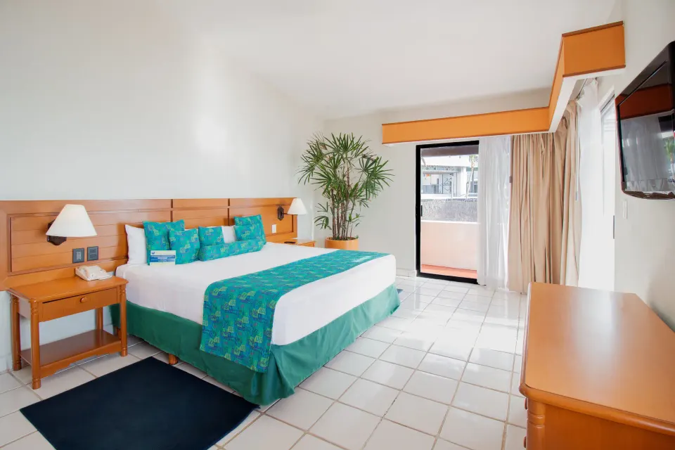 One-bedroom suite king bed with TV and balcony door at Plaza Pelicanos Club Beach Resort.