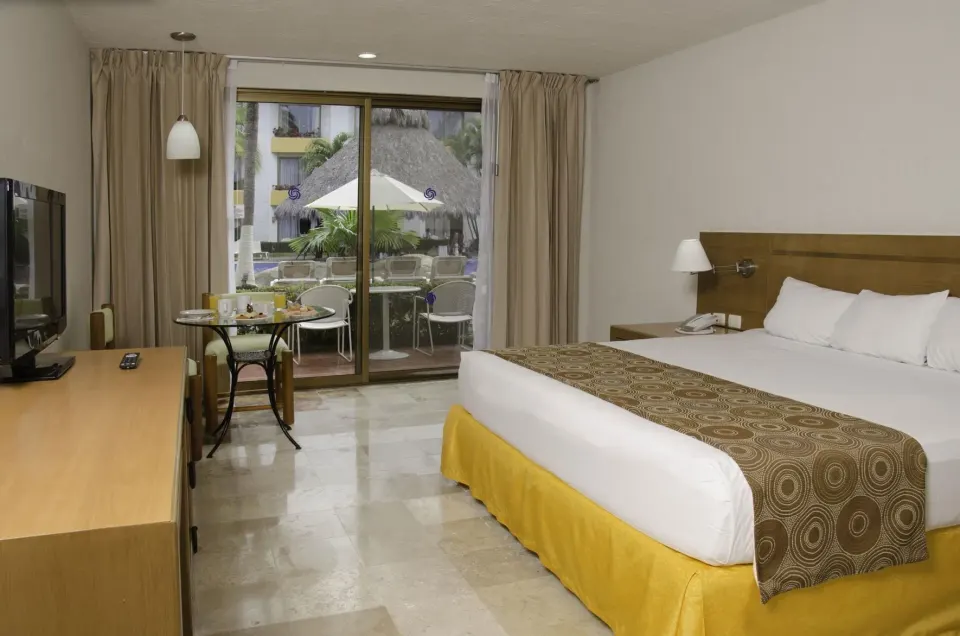 Superior room with king bed, TV, table, and balcony at Plaza Pelicanos Club Beach Resort.
