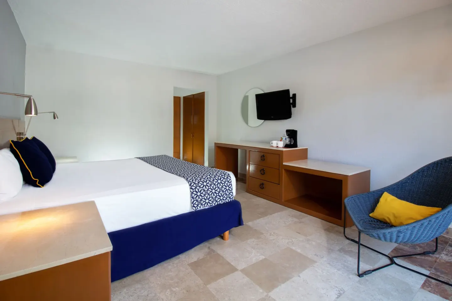 Superior Room king bed, dresser, TV and blue lounge chair at Plaza Pelicanos Club Beach Resort.