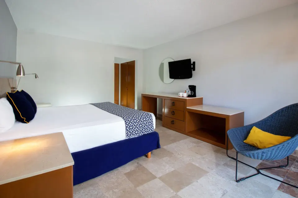 Superior Room king bed, dresser, TV and blue lounge chair at Plaza Pelicanos Club Beach Resort.