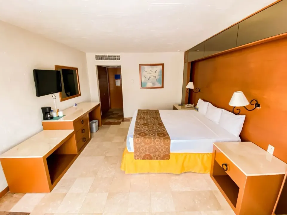 Superior room with king bed, desks, TV, and orange wood accents at Plaza Pelicanos Club Beach Resort.