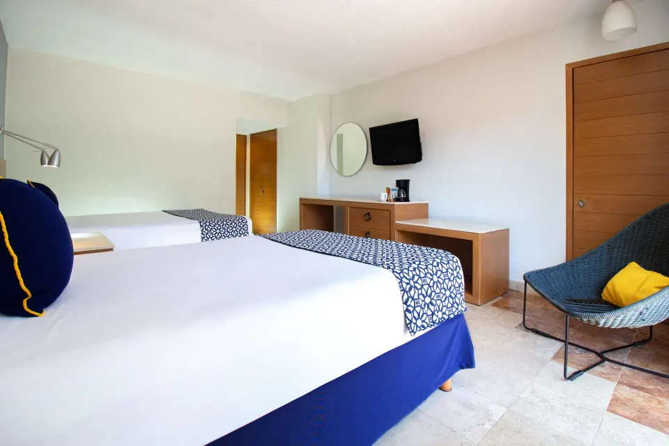 Superior Room with two beds, TV, desk, and lounge chair at Plaza Pelicanos Club Beach Resort.
