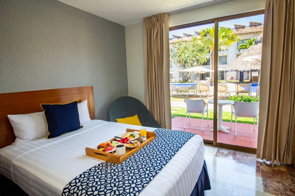 Superior king bed room at Plaza Pelicanos Club Beach Resort with breakfast tray and patio pool view.