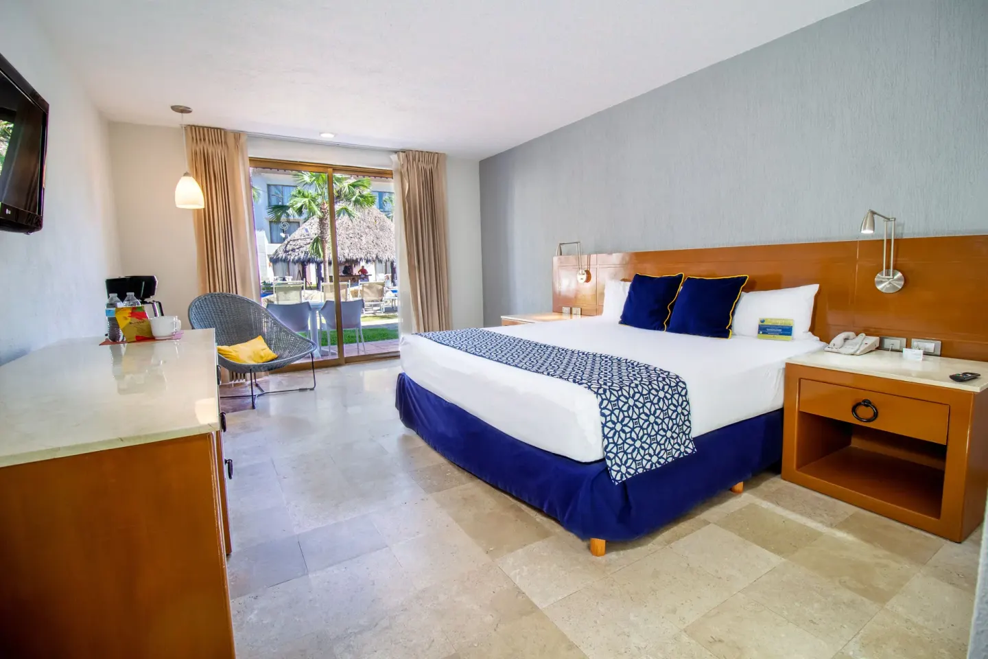 Superior king bed guest room at Plaza Pelicanos Club Beach Resort with patio doors and seating chair.