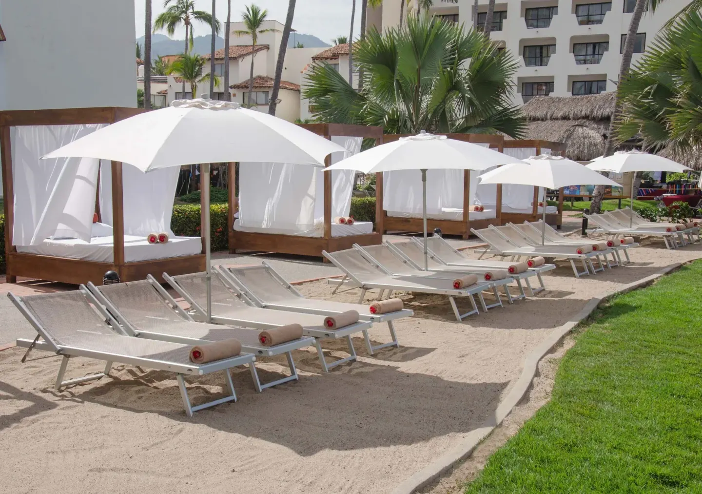 Cabana beds, loungers, and umbrellas on sand at Plaza Pelicanos Grand Beach Resort.