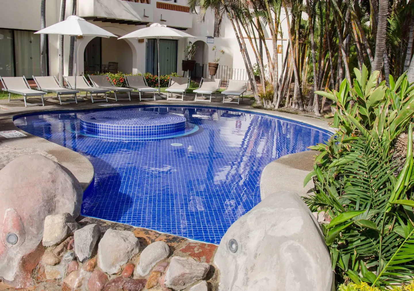 Blue-tiled courtyard pool with loungers at Plaza Pelicanos Grand Beach Resort.