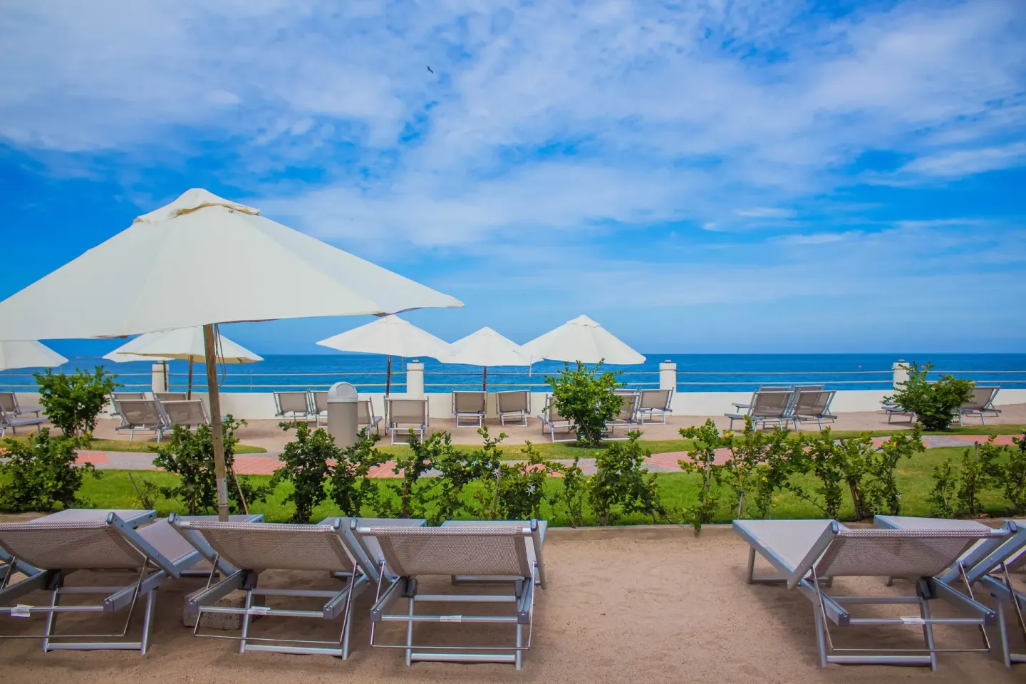 Oceanfront loungers and white umbrellas at Plaza Pelicanos Grand Beach Resort.