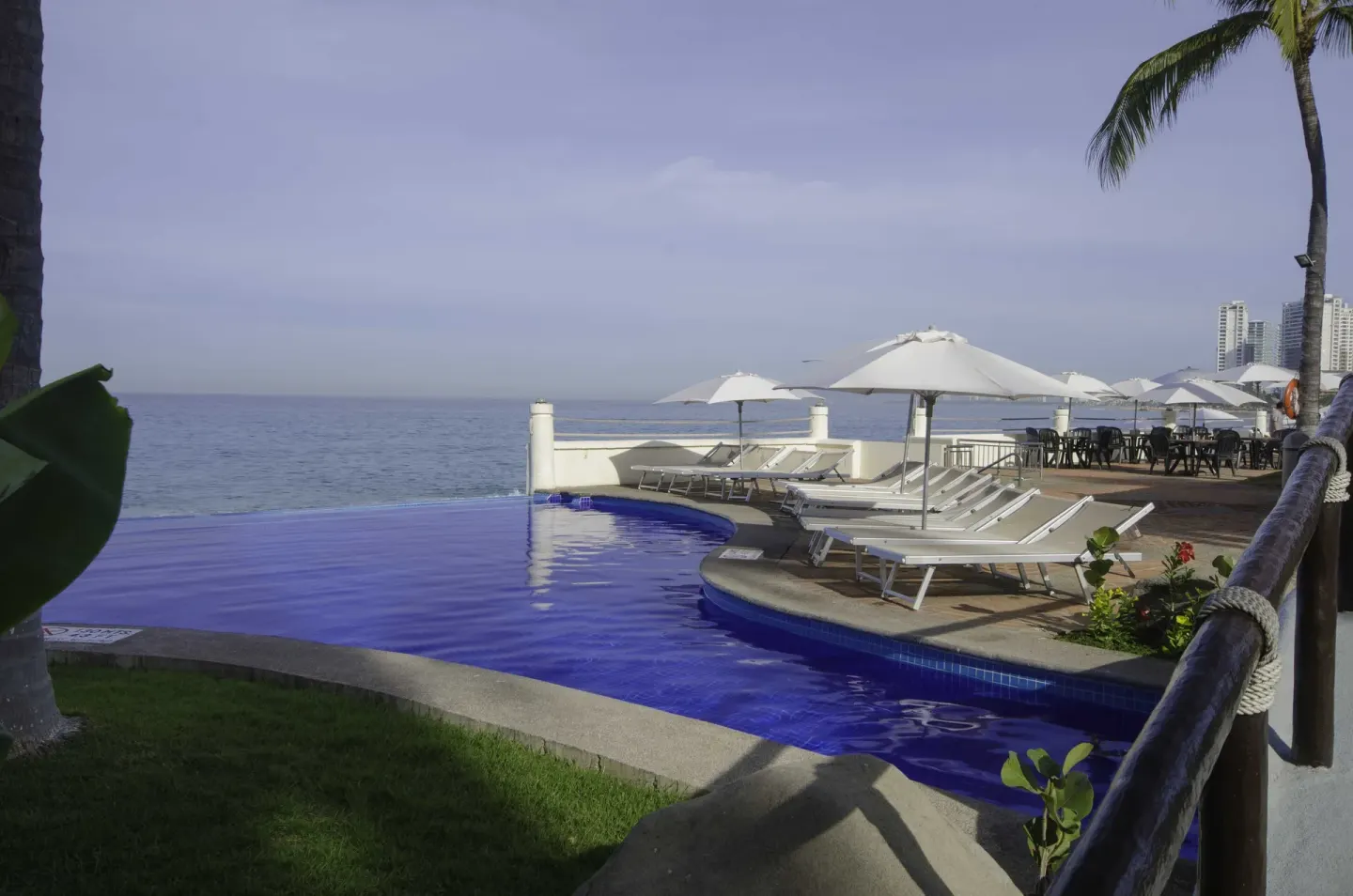 Poolside loungers and umbrellas by the ocean at Plaza Pelicanos Grand Beach Resort.