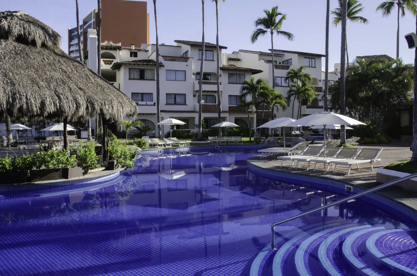 Pool with loungers and thatched shade at Plaza Pelicanos Grand Beach Resort.