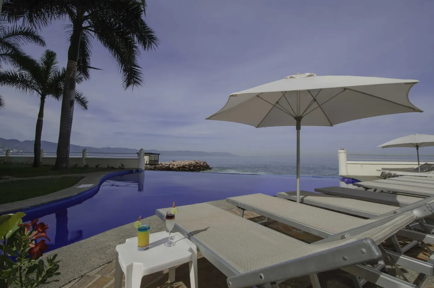 Loungers, umbrellas, and drinks beside the pool at Plaza Pelicanos Grand Beach Resort.