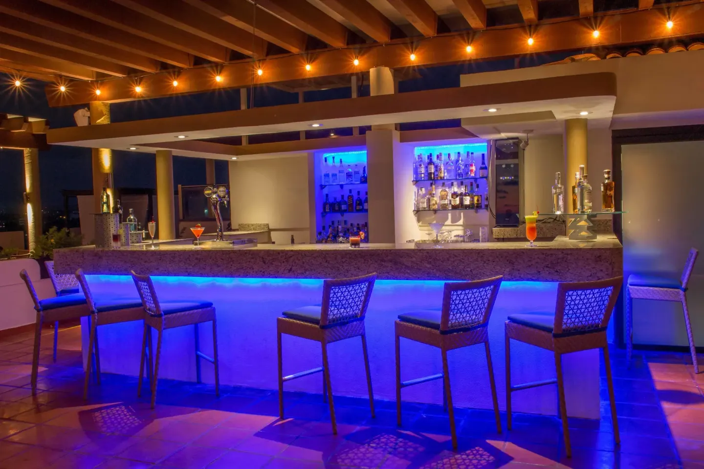 Blue-lit cocktail bar with high chairs at Plaza Pelicanos Grand Beach Resort.