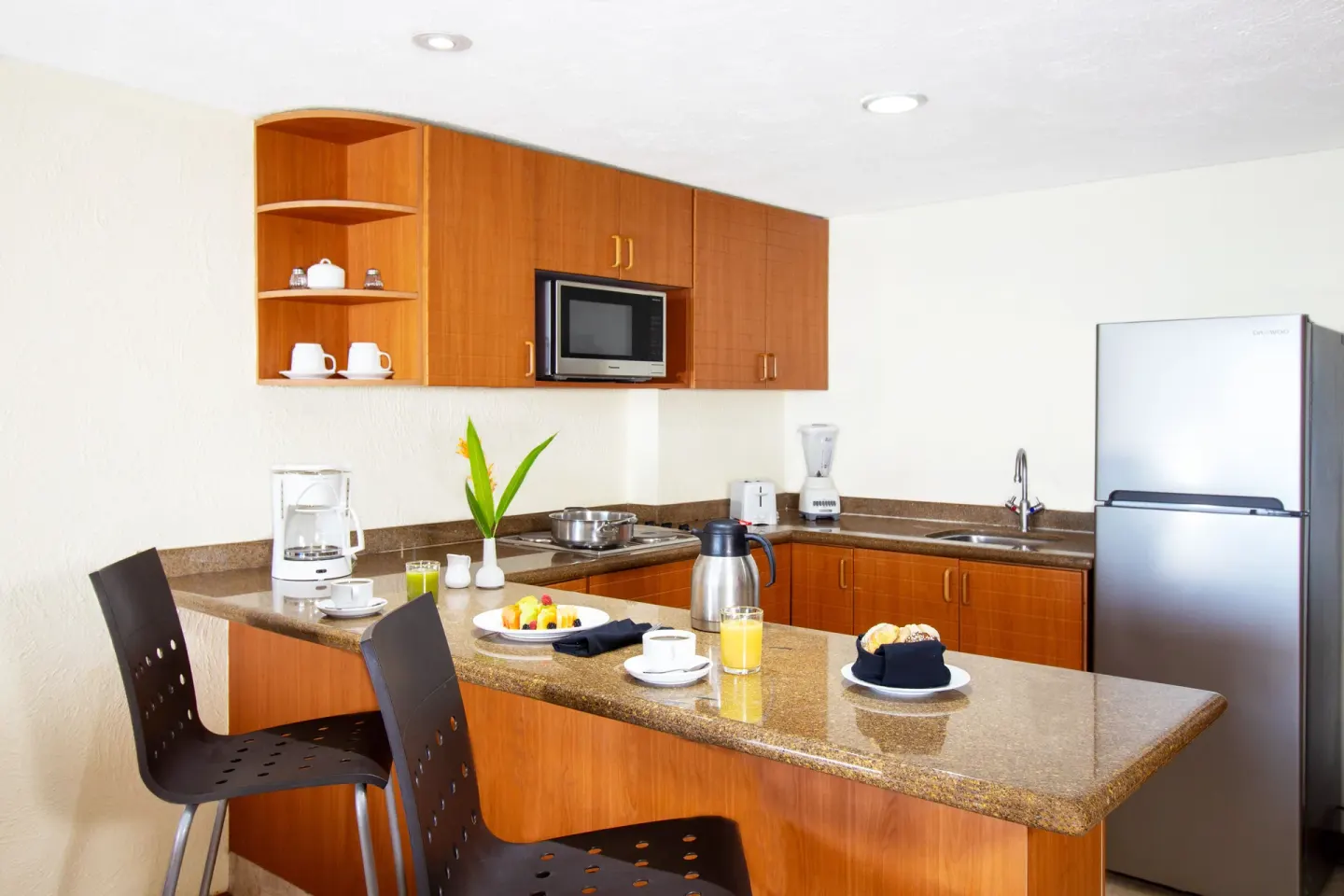 Suite kitchenette at Plaza Pelicanos Grand Beach Resort with counter seating, refrigerator, sink, and microwave.