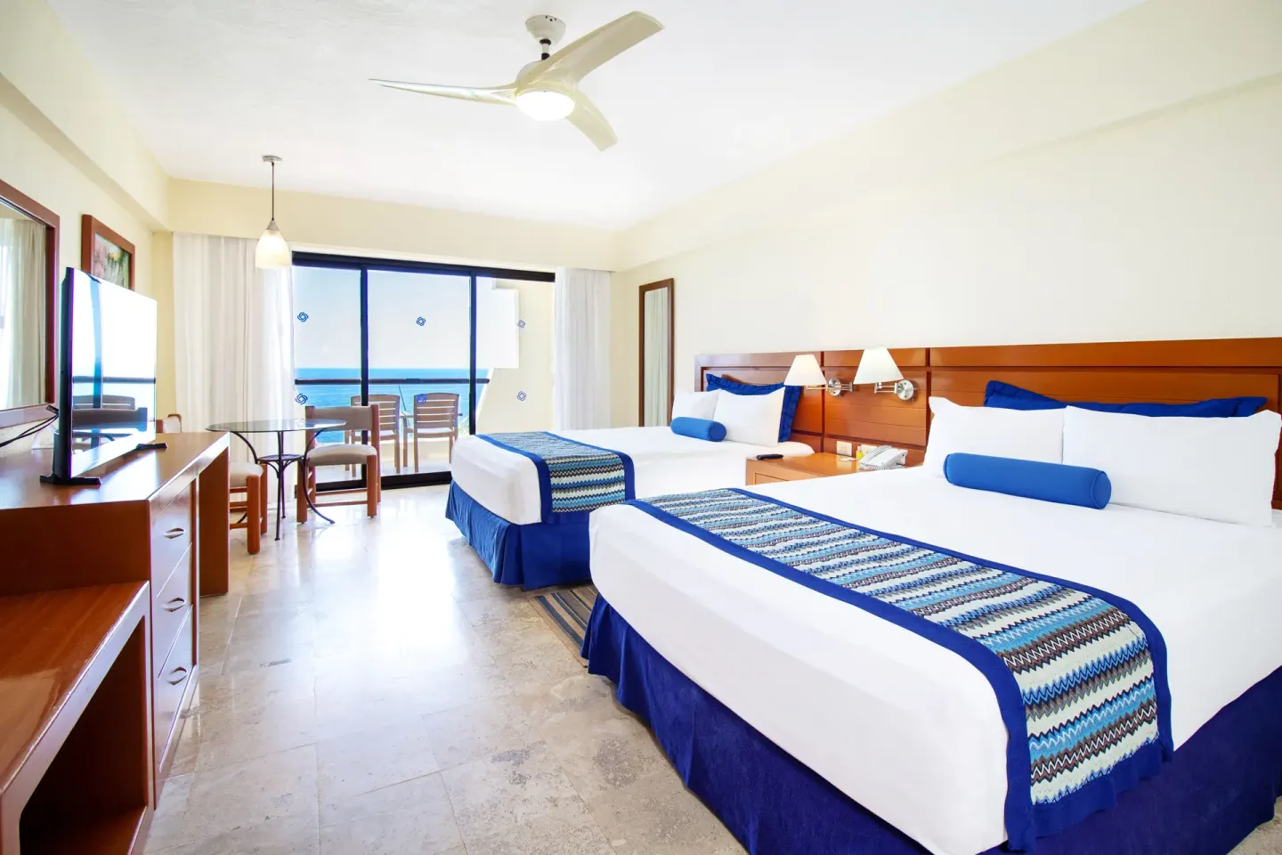 Two-bed ocean-view family suite at Plaza Pelicanos Grand Beach Resort with balcony seating and TV.