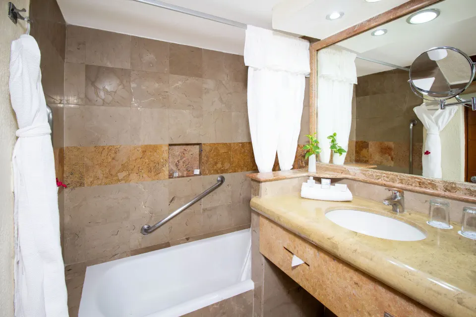 Bathroom with tub, vanity, mirror, and robe at Plaza Pelicanos Grand Beach Resort.
