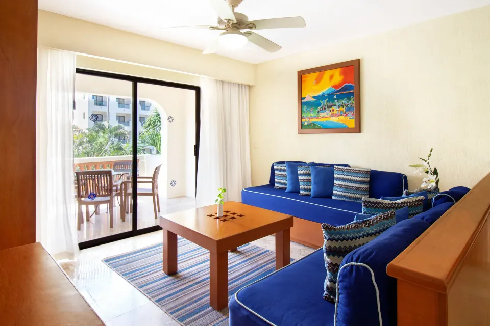 Living area with blue sofas and balcony doors at Plaza Pelicanos Grand Beach Resort.