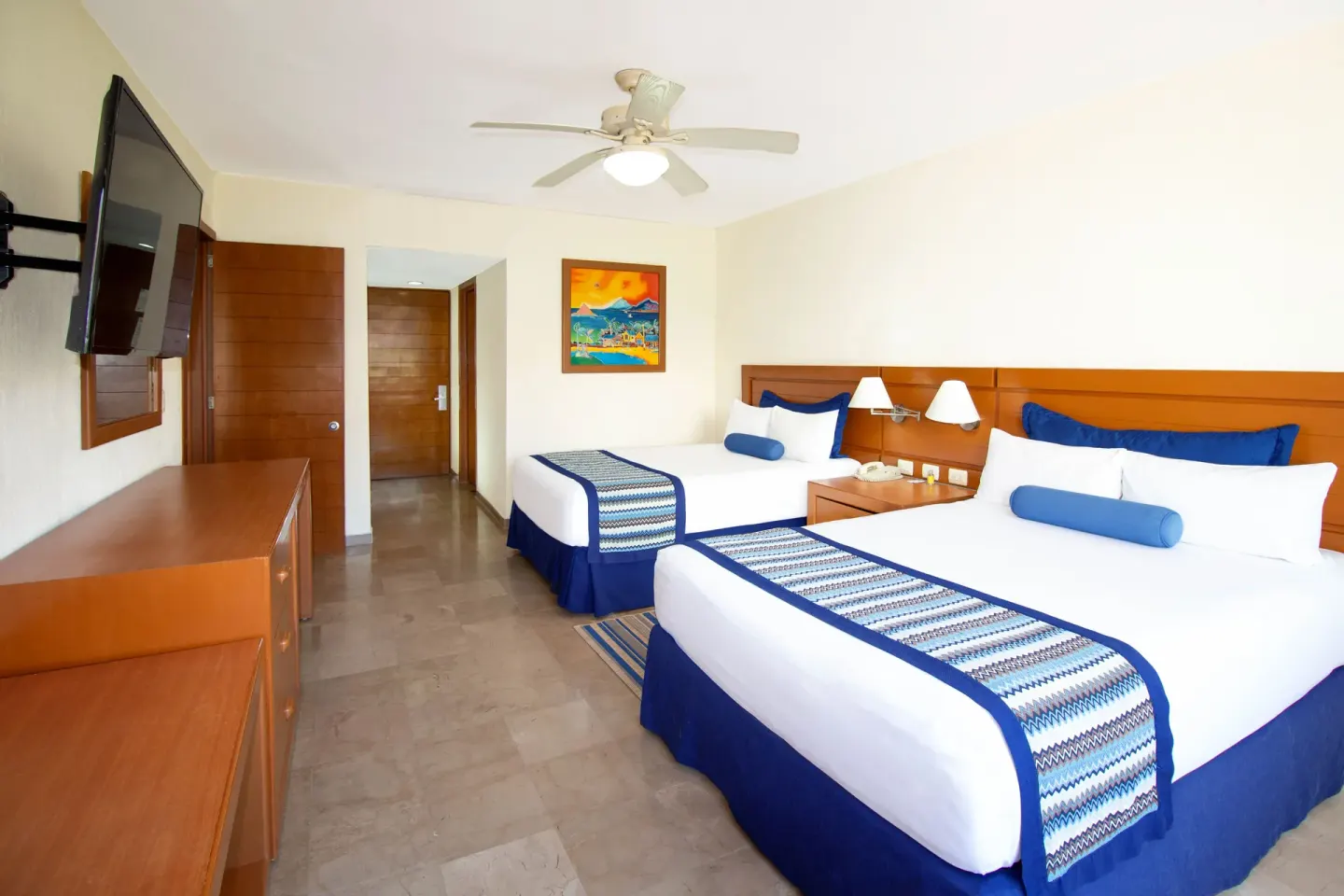 Family suite bedroom with two beds and wall-mounted TV at Plaza Pelicanos Grand Beach Resort.