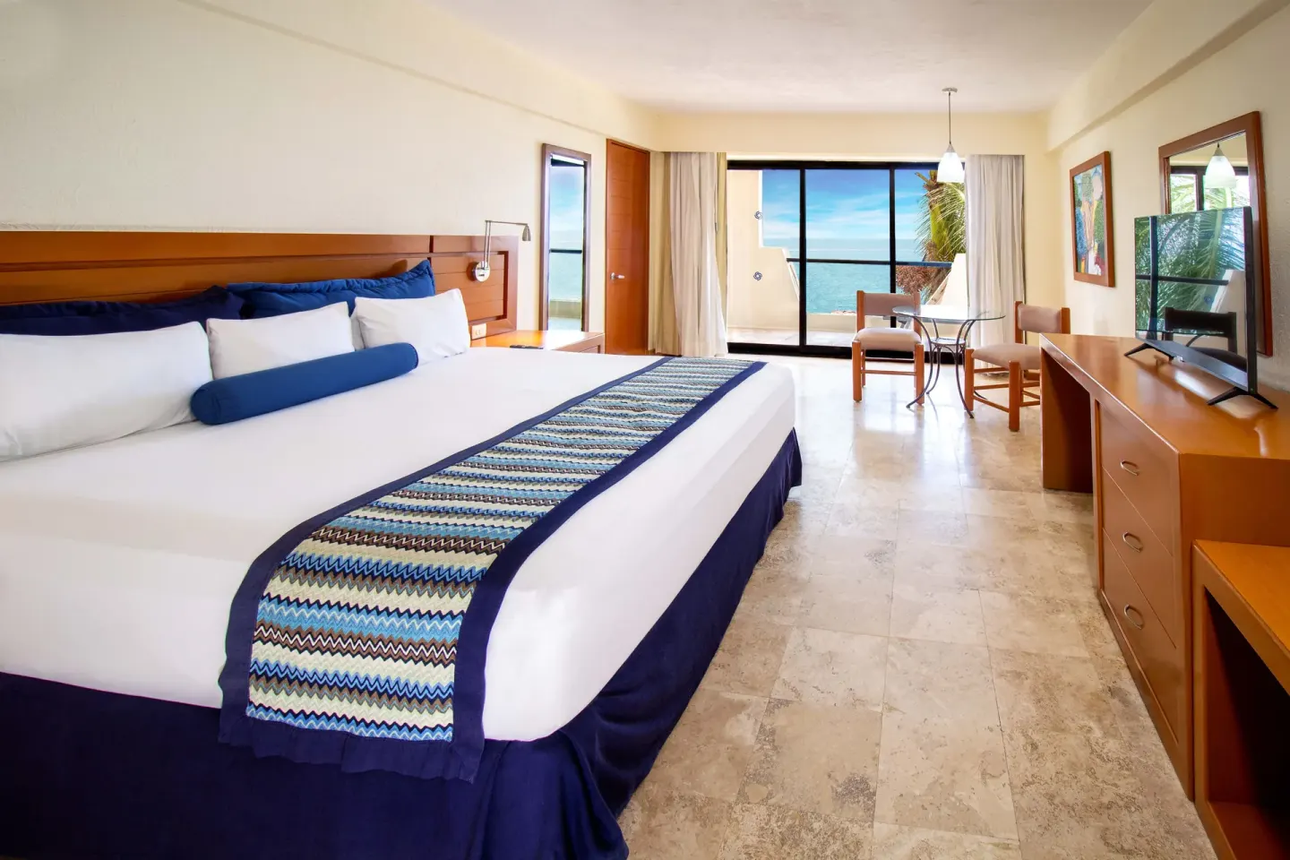 One Bedroom Suite Ocean View king bed, TV console, and balcony at Plaza Pelicanos Grand Beach Resort.