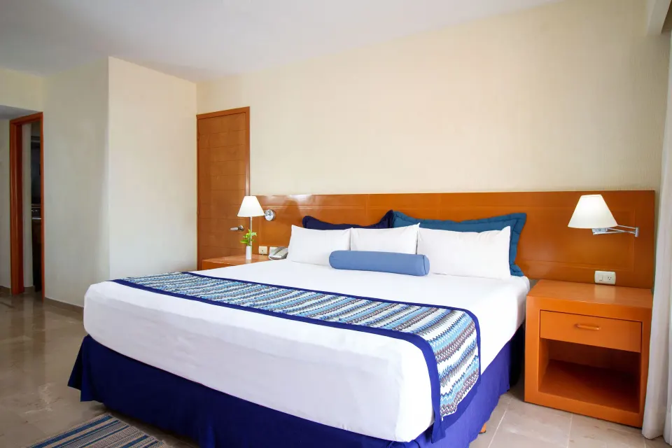 Standard Room king bed with blue accents at Plaza Pelicanos Grand Beach Resort.