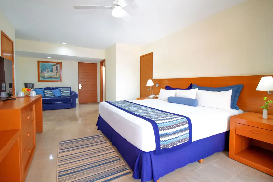 Standard Room king bed with sitting area and dresser at Plaza Pelicanos Grand Beach Resort.