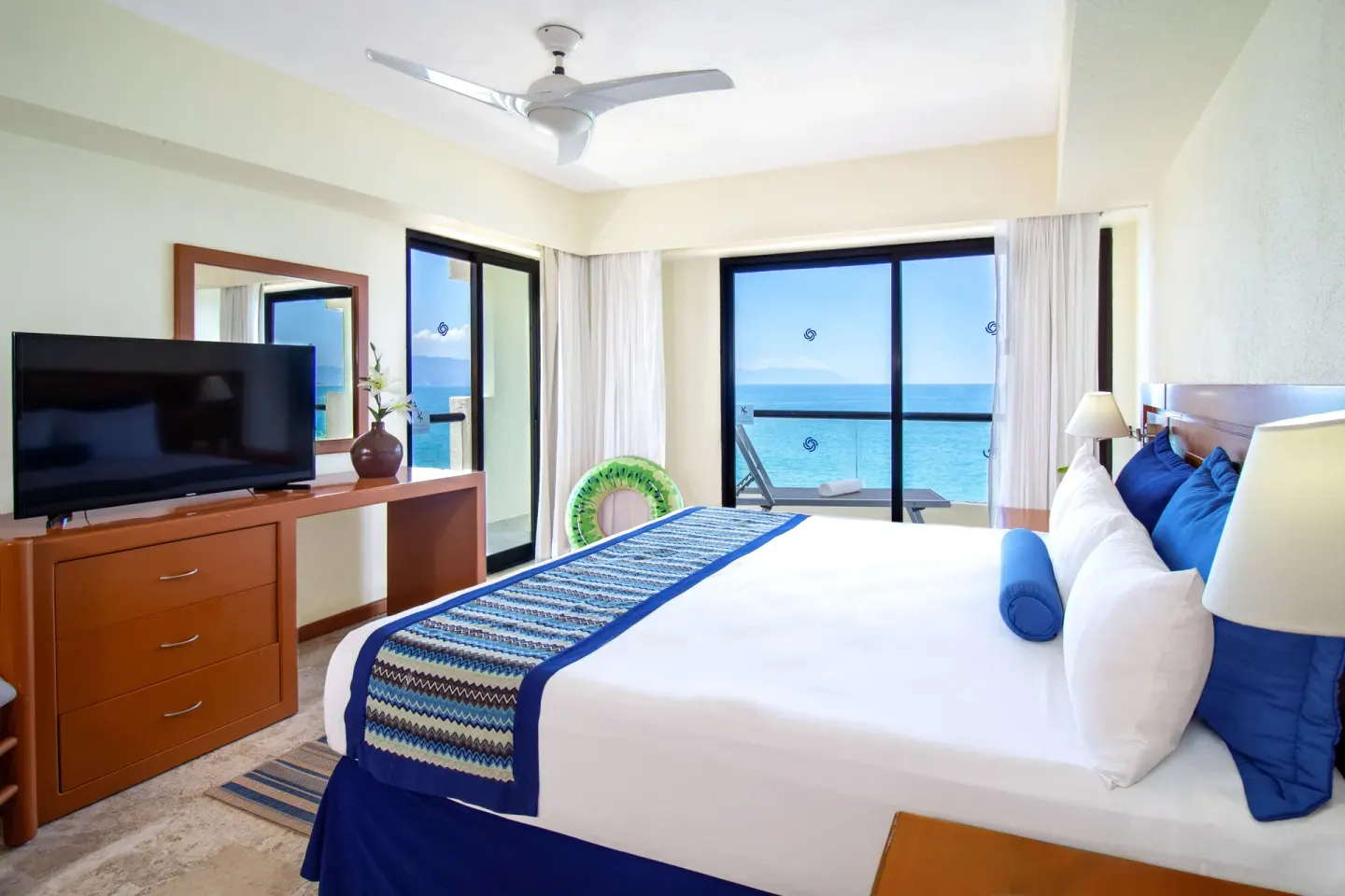 King bedroom with TV and ocean-facing balcony at Plaza Pelicanos Grand Beach Resort.