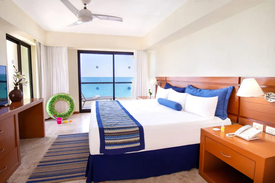 Ocean-view suite bedroom with king bed and balcony at Plaza Pelicanos Grand Beach Resort.