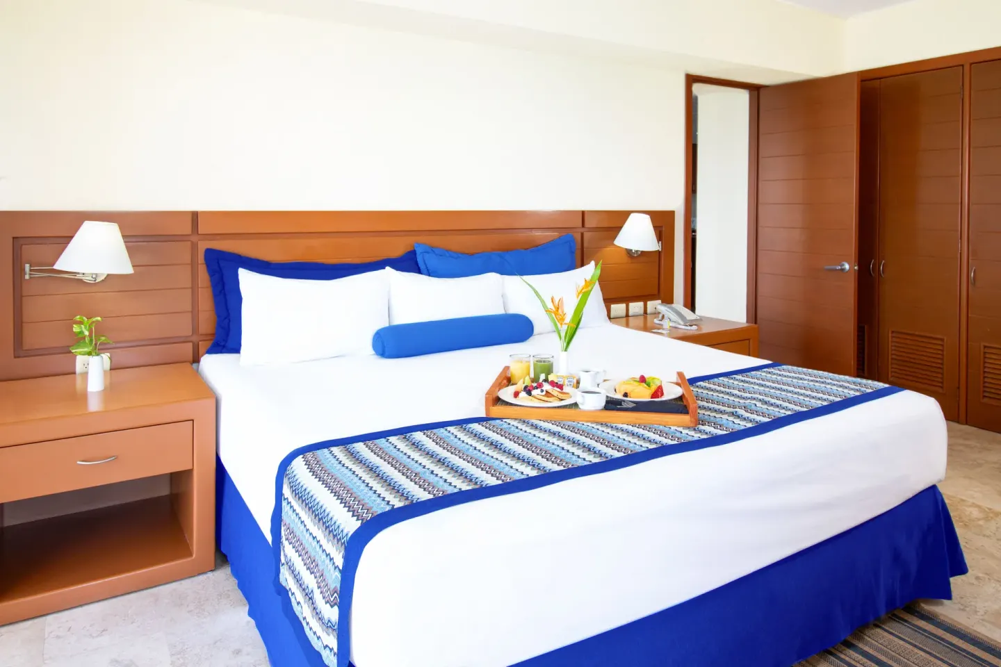 King bed with wood headboard in a Two Bedroom Family Suite at Plaza Pelicanos Grand Beach Resort.
