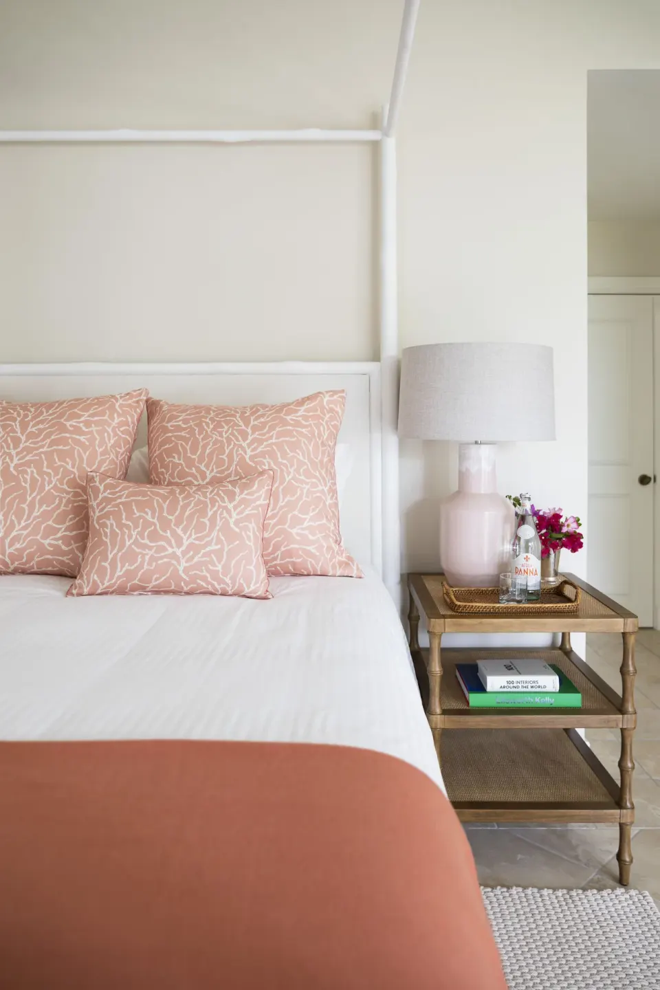 Close view of a four-poster bed with coral pillows and bedside table at Point Grace.