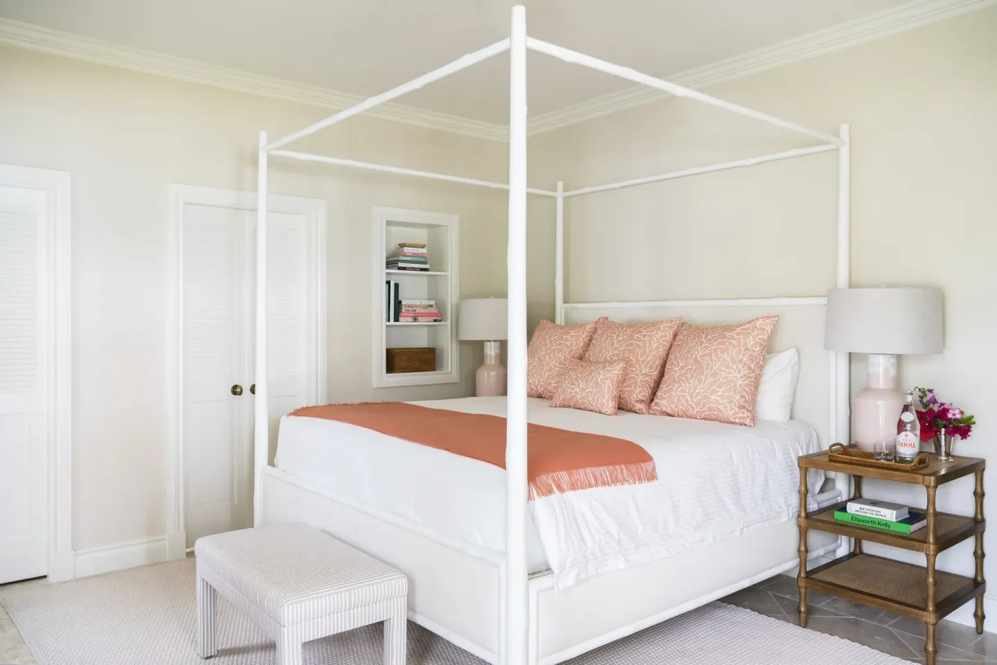 White four-poster bed with coral accents, bench, and bedside tables at Point Grace.