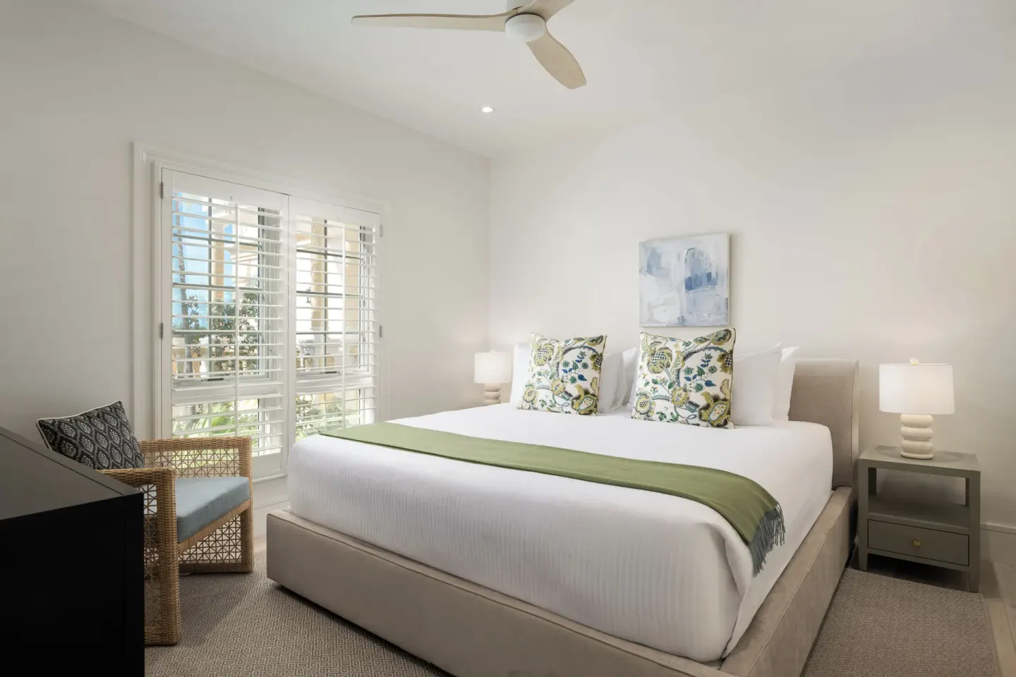 Guest room with king bed, wicker chair and shuttered doors at Point Grace.