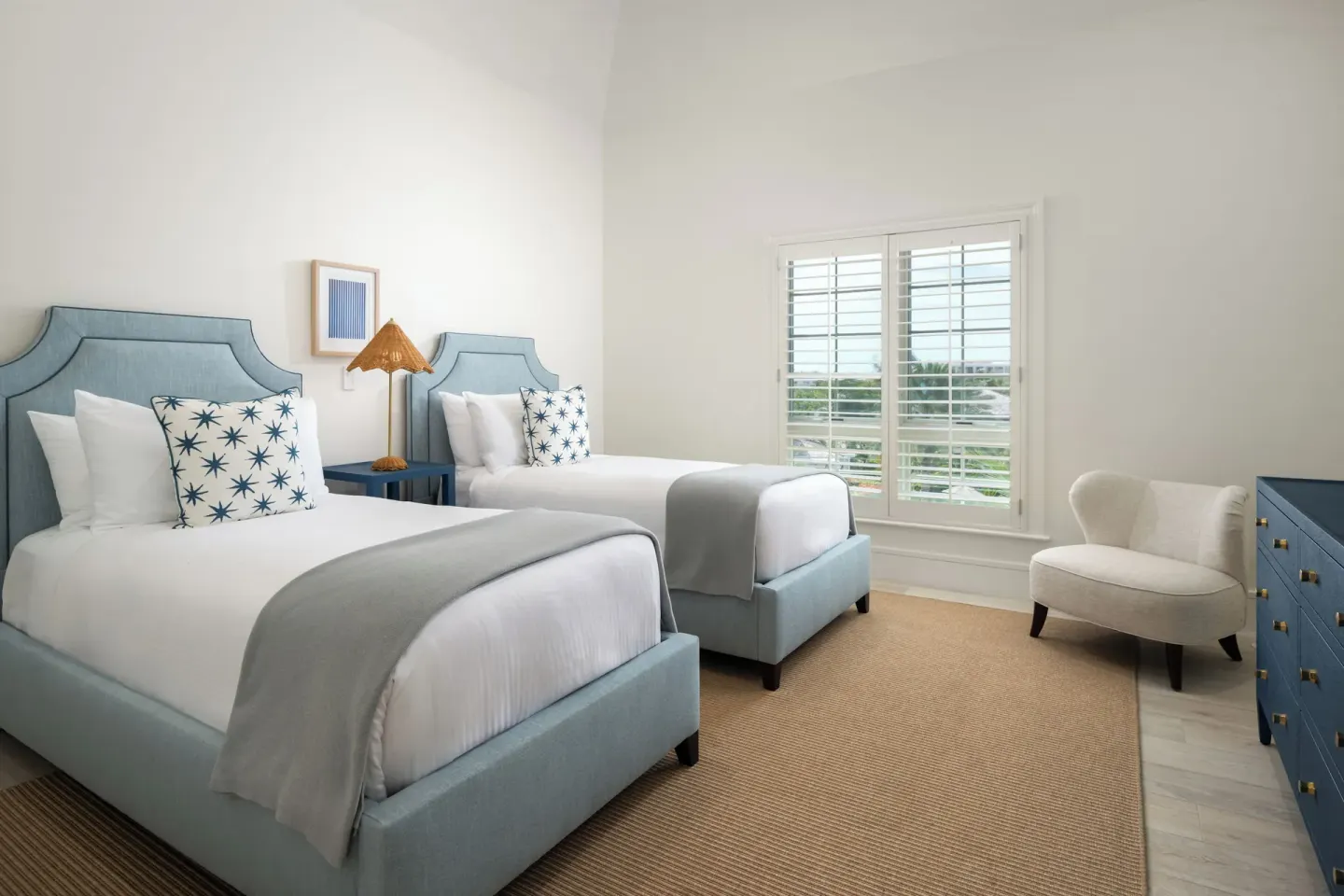 Guest room with two twin beds, blue headboards and a window at Point Grace.