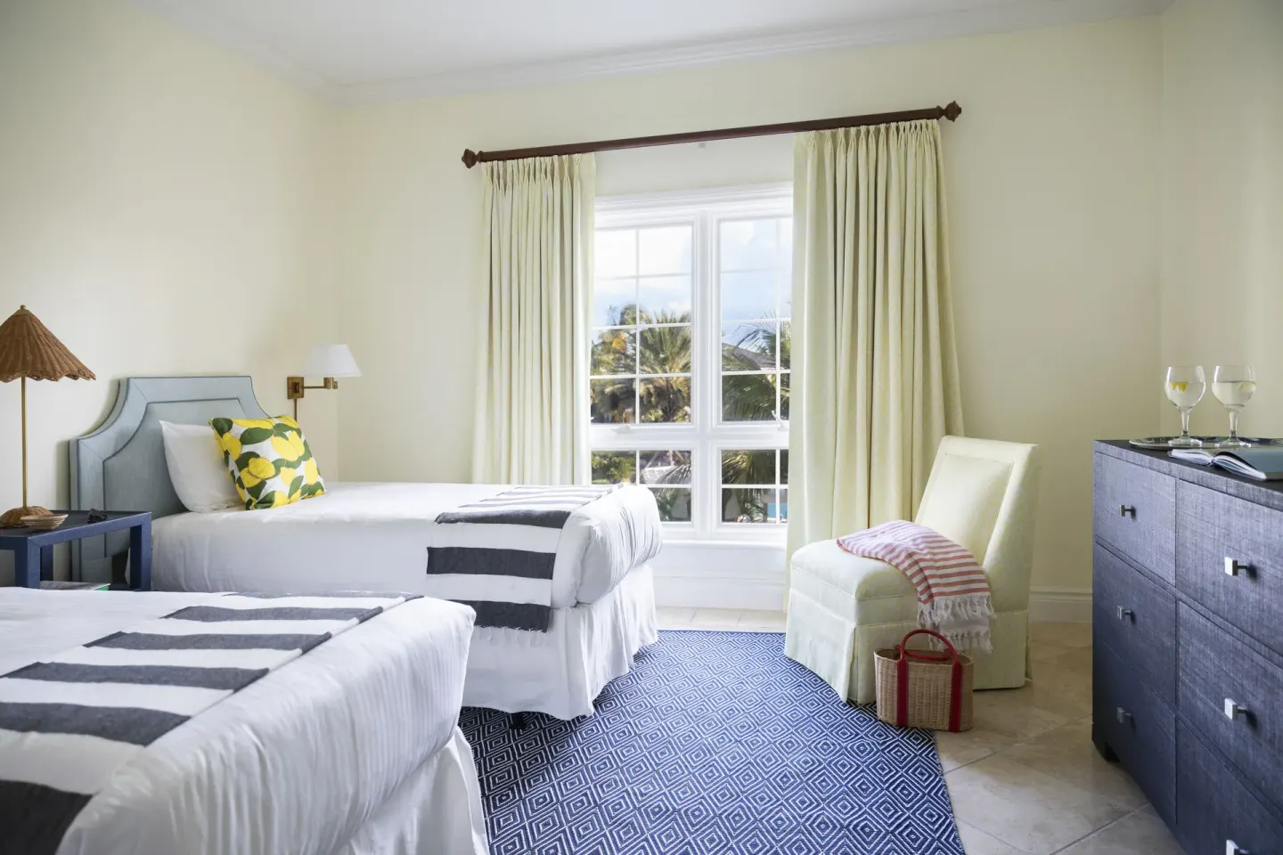 Twin-bed guest room with blue rug, dresser, and palm-view window at Point Grace.