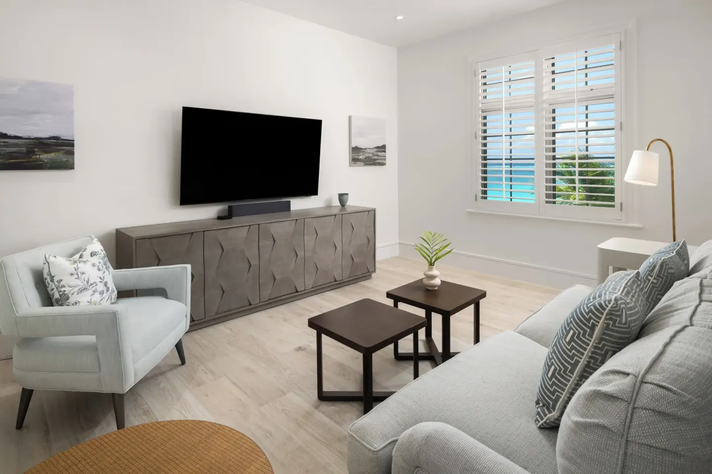 Guest suite sitting room with TV, sofa, armchair, and ocean-view shutters at Point Grace.